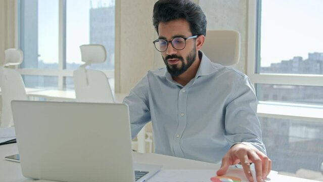 Arabian Indian man muslim male businessman entrepreneur professional executive worker manager working with laptop in office check information financial graphs read papers business documents paperwork