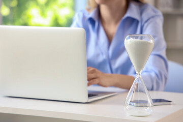 Hourglass on table of businesswoman working in office, closeup