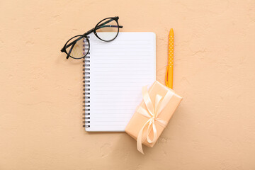 Gift box with notebook and eyeglasses on orange background