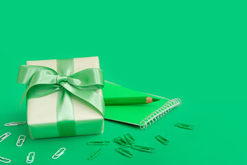 Gift box with paper clips, notebook and pencil on green background