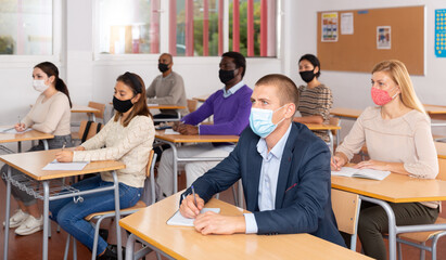 Obraz na płótnie Canvas Portrait of confident young adult male wearing face mask for viral protection studying in classroom with colleagues