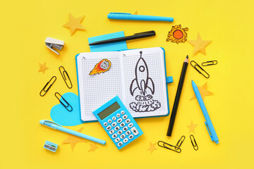 Notebook with drawn rocket, calculator and different stationery on yellow background