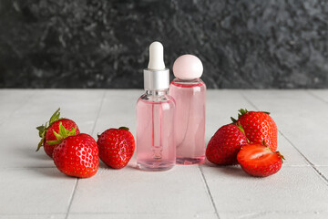 Bottles with cosmetic oil and strawberries on white tile table