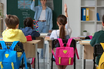 Little pupils with backpacks having lesson in classroom, back view