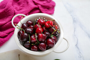 Colander with sweet cherries on white background
