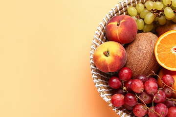 Naklejka na ściany i meble Wicker bowl with different fresh fruits on orange background