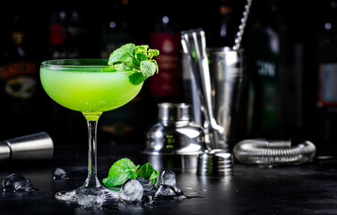 Last word alcohol cocktail drink with dry gin, herbal liqueur, lime juice and ice. Black bar counter background, steel bar tools and bottles