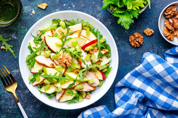 Waldorf salad with fresh apple, celery, lettuce, grilled chicken fillet, arugula and walnuts on plate, blue table background, top view