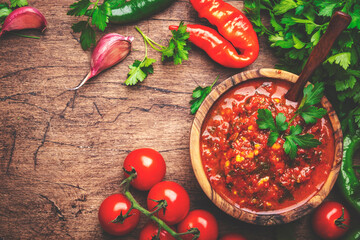 Traditional armenian spicy adjika sauce with hot pepper, paprika, tomatoes, garlic and parsley on rustic wooden kitchen table background, top view