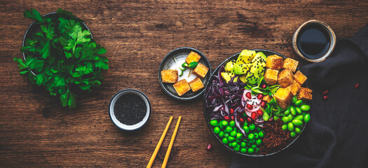 Obraz na płótnie Canvas Vegan buddha bowl with red quinoa, fried tofu, avocado, edamame beans, green peas, radish, red cabbage and sesame seeds with soy sauce. Healthy diet food. Wood kitchen table background, top view