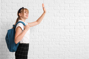 Female student with backpack waving hand on white brick background