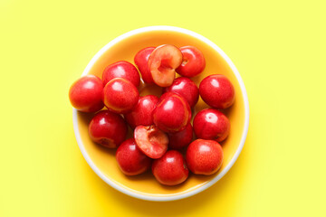 Plate with sweet cherries on yellow background