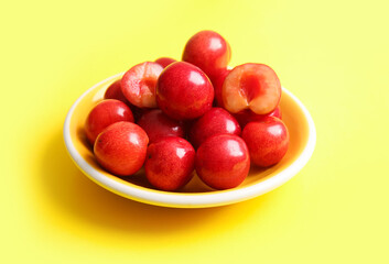 Plate with sweet cherries on yellow background