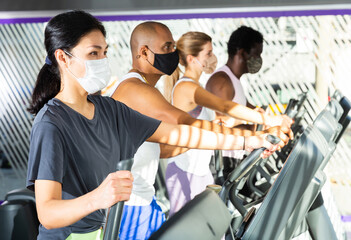 Portrait of young adult woman training on elliptical cross trainer in gym, all people wearing face...