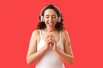 Obraz na płótnie Canvas Young woman in headphones with lollipop showing tongue on red background