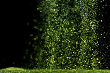 Explosion metallic green glitter sparkle. Green Glitter powder spark blink celebrate, blur foil explode in air, fly throw green glitters particle. Black background isolated, selective focus Blur bokeh