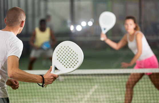 Rear view of man with white racket playing padel tennis with friends at court