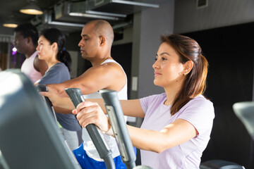Young adult woman doing cardio workout using elliptical cross trainer at fitness center