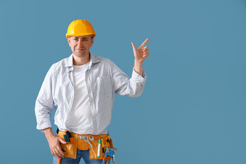 Mature builder with tool belt pointing at something on blue background