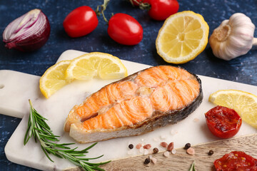 Board with tasty grilled salmon steak on blue background