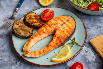 Plate with tasty grilled salmon steak and vegetables on blue background
