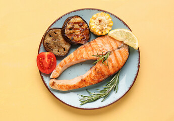 Plate with tasty grilled salmon steak and vegetables on yellow background