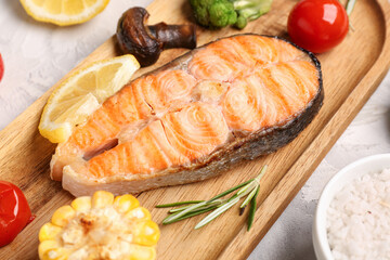 Wooden board with tasty grilled salmon steak and vegetables on grunge background