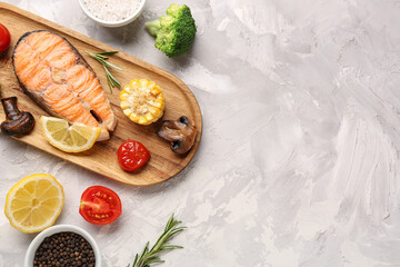 Wooden board with tasty grilled salmon steak and vegetables on grunge background