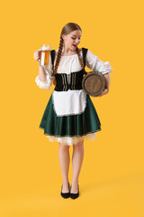 Surprised Octoberfest waitress with beer and barrel on yellow background