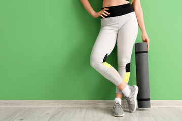 Fototapeta na wymiar Young woman in sportswear and with yoga mat near green wall