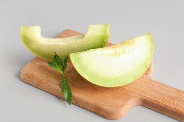 Wooden board with pieces of sweet melon and mint on grey background