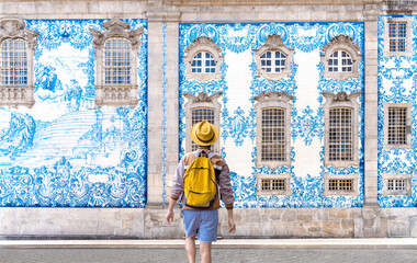 Traveler man with hat and yellow backpack visiting Porto in Portugal - Young tourist enjoy the painted blue tile wall at Carmo church in Clerigos, Porto - City vacation travel concept