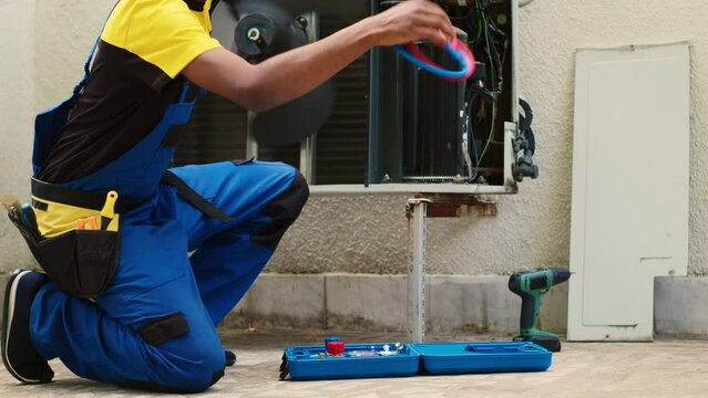 Skilled wireman doing routine air conditioner maintenance, assembling pressure measurement device before starting work. Capable specialist refilling cooling system freon tank