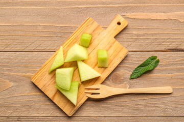 Board with pieces of sweet melon and mint on wooden background