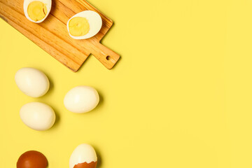 Tasty boiled eggs and wooden board with halves on yellow background