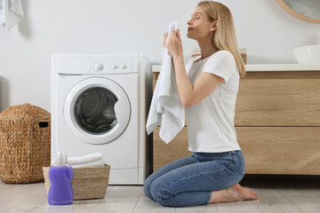 Woman smelling clean towels and sitting on floor near washing machine in bathroom, space for text