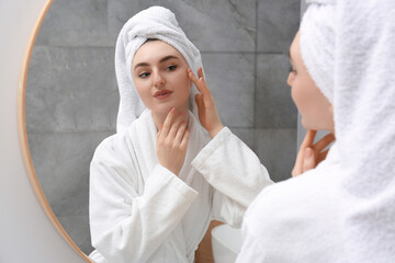 Beautiful woman wearing white robe and looking in mirror in bathroom