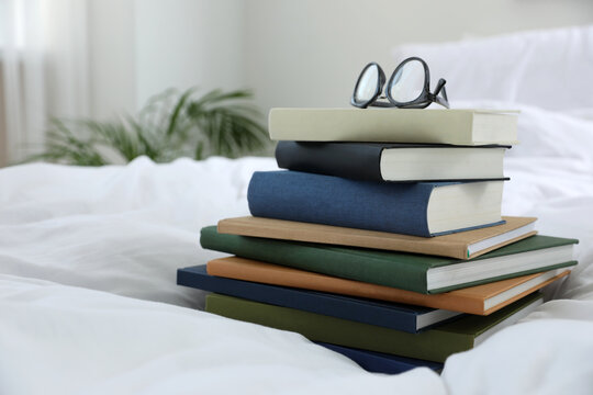 Hardcover books and glasses on bed indoors