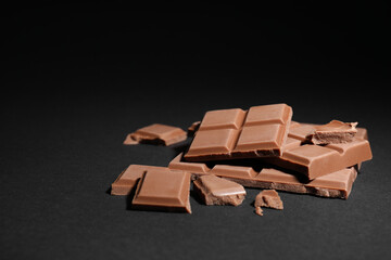 Pieces of delicious milk chocolate bars on black background
