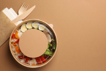 Tasty food in container with wooden fork and knife on beige background, flat lay. Space for text