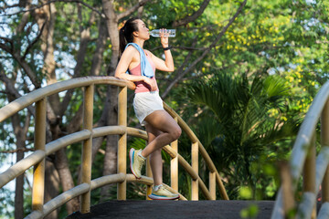 Healthy woman drinks water after workouts running exercise in the park in summer