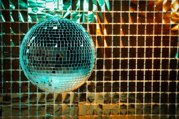 Shiny disco ball against foil party curtain under turquoise and orange light, space for text