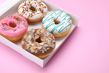 Box with different tasty glazed donuts on pink background. Space for text