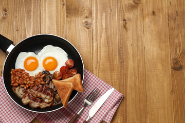 Frying pan with cooked traditional English breakfast on wooden table, flat lay. Space for text