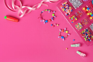 Handmade jewelry kit for kids. Colorful beads, ribbon and bracelets on bright pink background, flat lay. Space for text