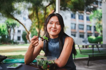 Fotobehang Smiling college student girl eating a healthy salad while taking a break with her friends © Pablo Rasero