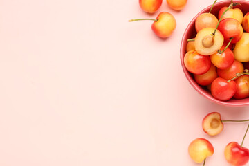 Bowl with sweet yellow cherries on pink background
