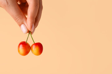 Woman holding sweet yellow cherries on orange background