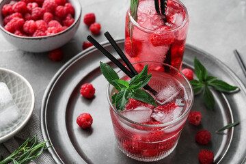 Glasses of fresh raspberry lemonade and bowl with berries on grey table