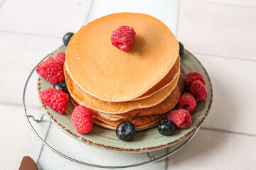Plate of tasty pancakes with raspberries and blueberries on white tile background